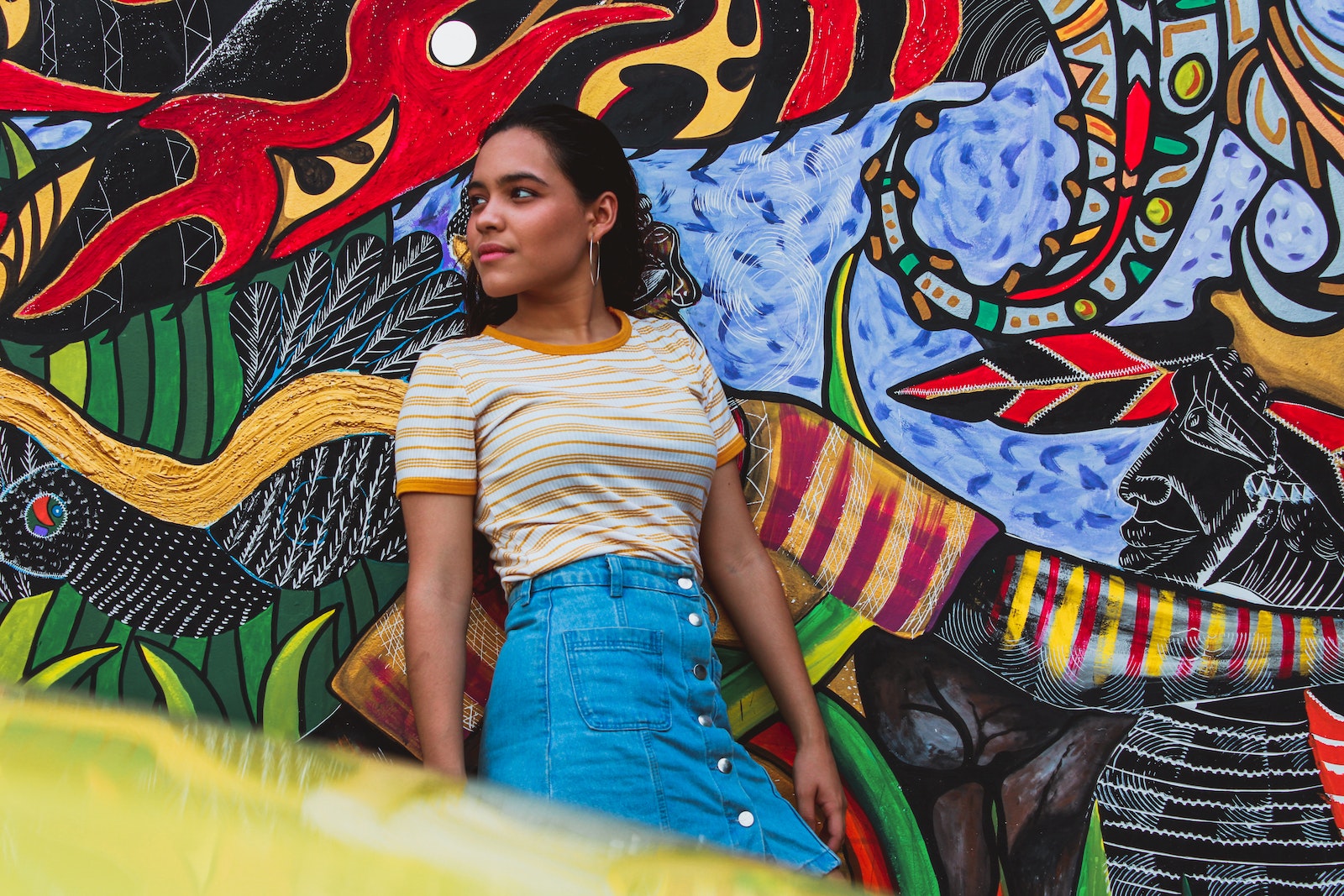 Una mujer recostada sobre una pared con un graffiti de fondo.