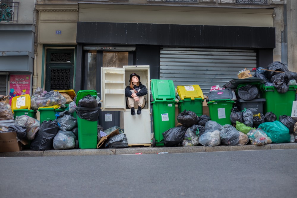 Una mujer sentada dentro de un refigerador en una montaña de basura en la calle. 