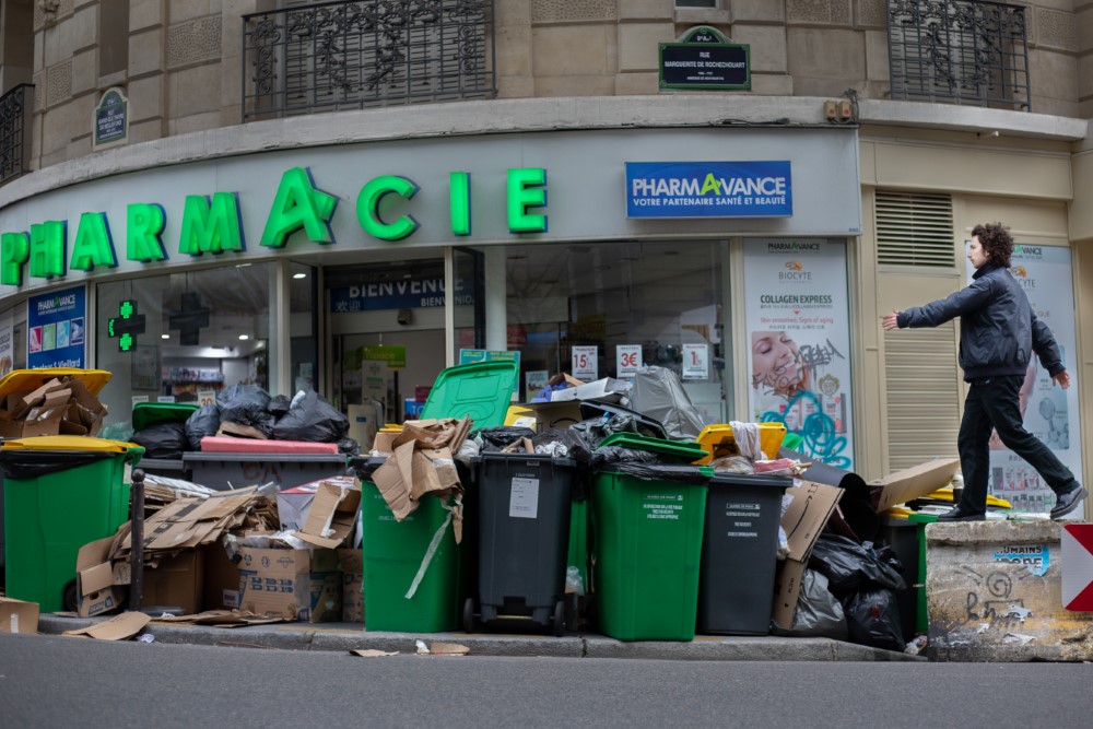 Una calle de París llena de basura. Una farmacia se ve al fondo.