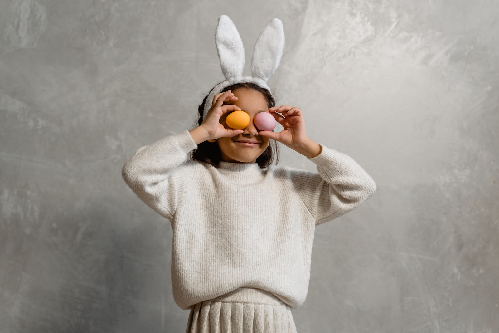 Girl wearing Easter bunny Headwear covering her Eyes with Easter Eggs
