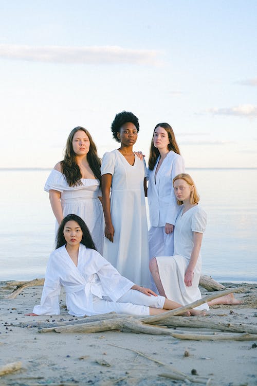 Un grupo de cinco mujeres en la playa, todas llevan vestido blanco.