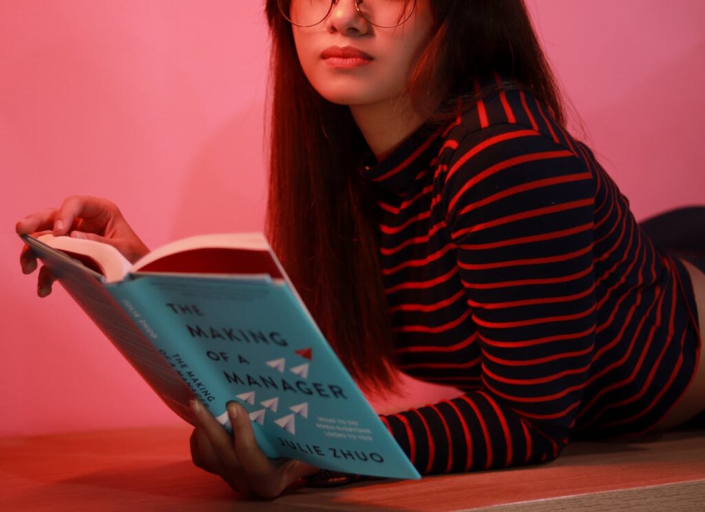 Una chica acostada en el piso mientras lee un libro.